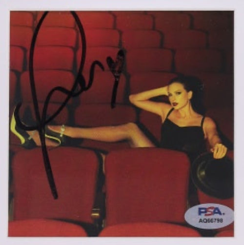 An autographed photo print of taylor swift reclining in red theater seats, with a black signature across the left side and a PSA/DNA authentication sticker in the bottom right corner
