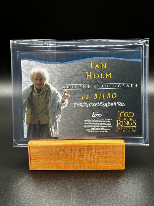 Autograph card of Ian Holm as Bilbo with a display stand on a dark background