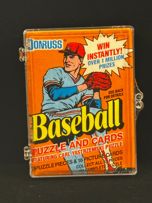 A vintage Donruss Baseball Puzzle and Cards set in a clear plastic case, featuring a bright orange cover with a baseball player illustration and bold yellow 'Baseball' text, photographed against a black background.