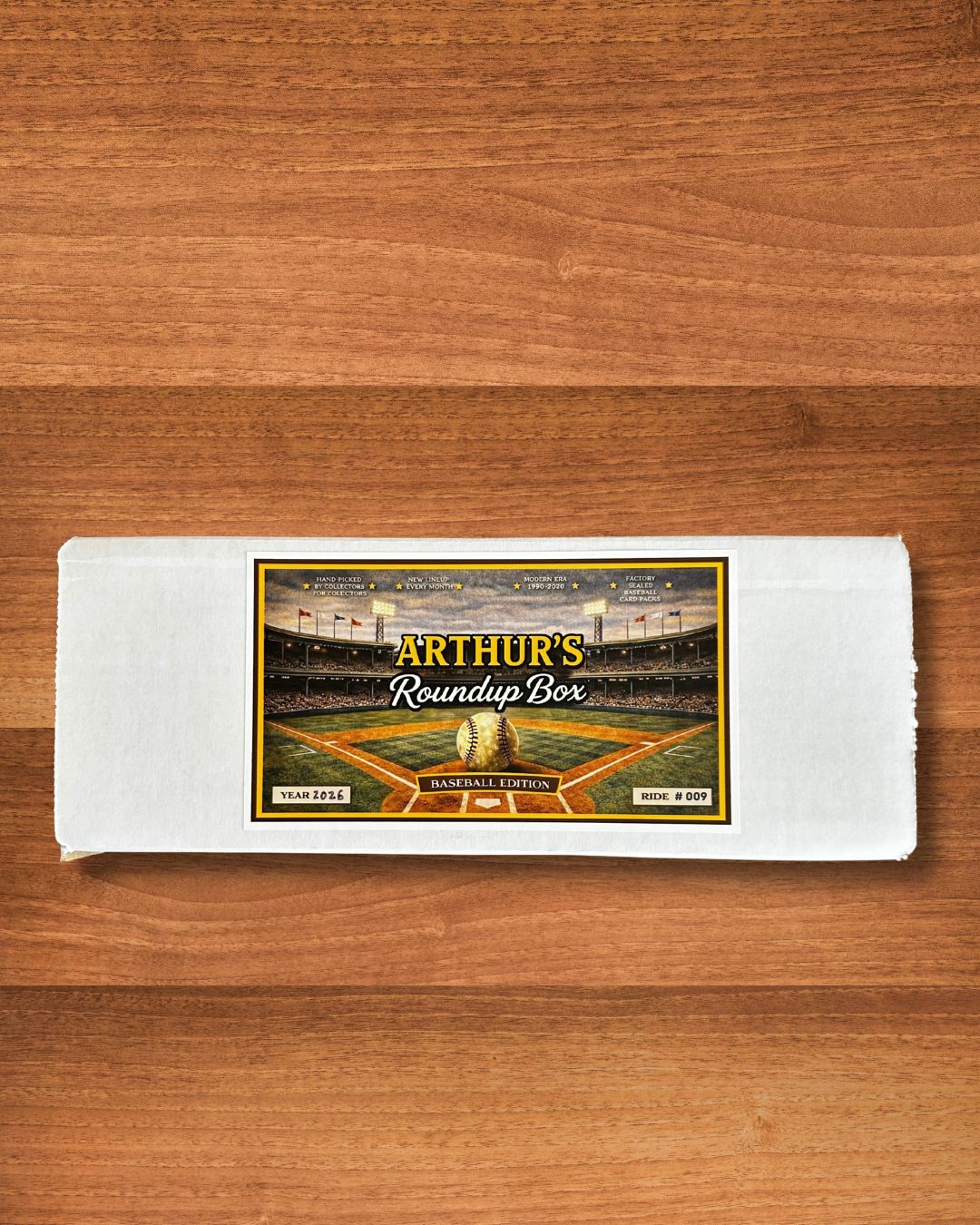 A white rectangular box with a baseball stadium label reading 'Arthur's Roundup Box' and 'Baseball Edition' on a wooden surface.