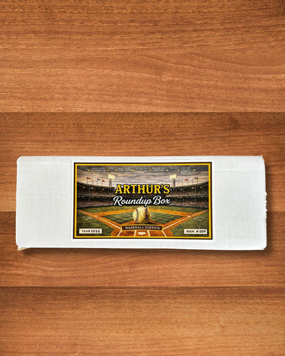 A white rectangular box with a baseball stadium label reading 'Arthur's Roundup Box' and 'Baseball Edition' on a wooden surface.