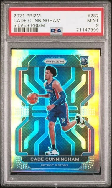 A PSA graded 2021 Prizm Silver Prizm basketball card of Cade Cunningham, showing him in a Detroit Pistons uniform on a holographic blue and gold background.