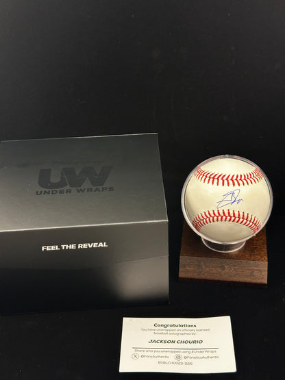 A Jackson Chourio autographed baseball displayed in a clear sphere on a wooden stand, alongside a black Fanatics Under Wraps presentation box and a small white congratulations card on a black background.