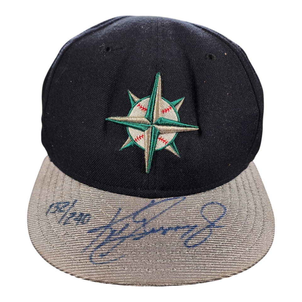 A black and gray mariners baseball cap featuring an embroidered green and white compass star logo on the front, with a blue autograph of ken griffey jr. on the brim.