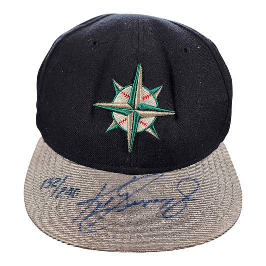 A black and gray mariners baseball cap featuring an embroidered green and white compass star logo on the front, with a blue autograph of ken griffey jr. on the brim.