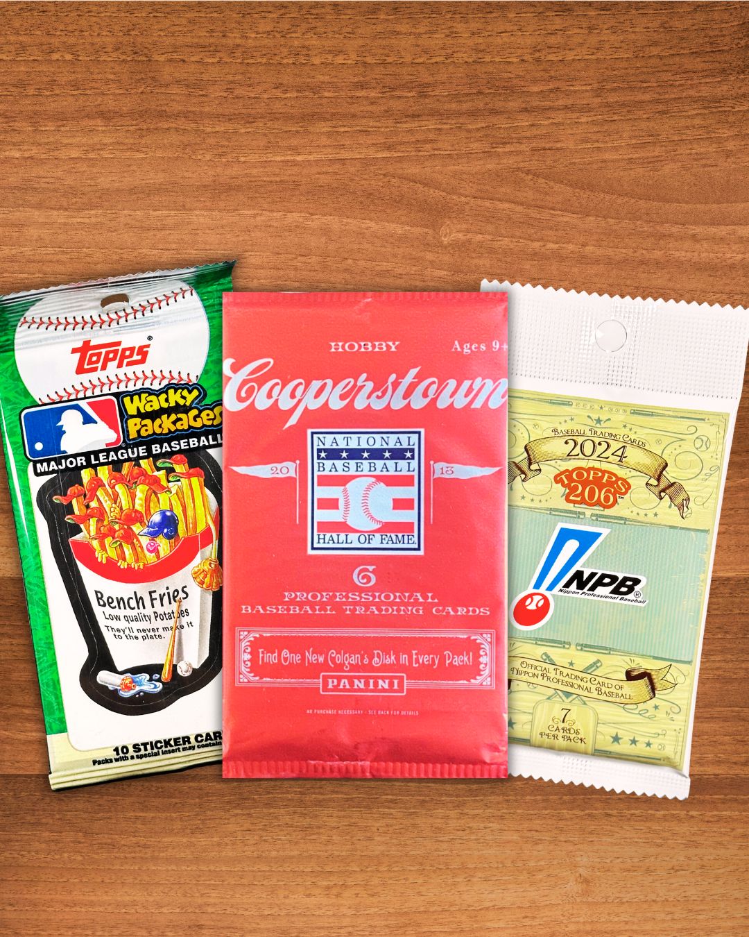 Three vintage baseball trading card packs arranged on a wooden surface: a green and white Topps Wrapper Pack on the left, a red Cooperstown National Baseball Hall of Fame Panini pack in the center, and a white and green NPB 2024 Rookie Pack on the right.