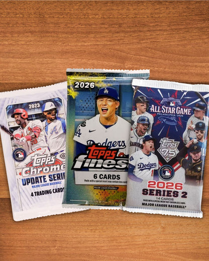 Three Topps baseball trading card packs arranged on a wooden surface: a 2023 Chrome Update Series pack, a 2026 Topps Fines 6-card foil pack, and a 2026 Series 2 All Star Game pack.
