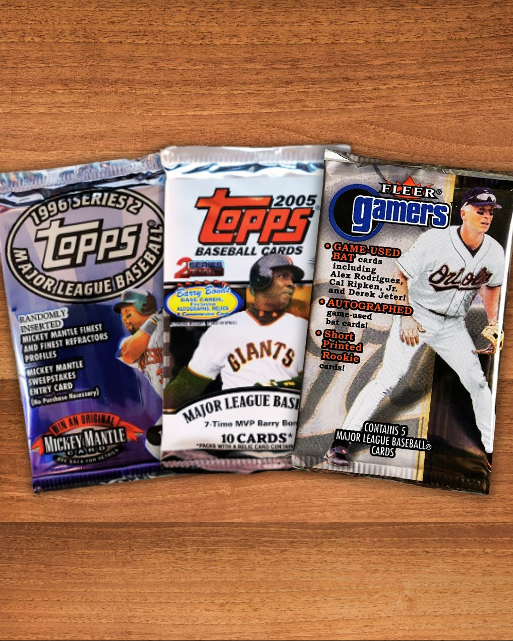 Three sealed baseball trading card booster packs arranged side by side on a wooden tabletop: a 1995 Topps Major League Baseball pack, a 2005 Topps pack, and a Fleer Gamers baseball card pack.