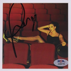 An autographed photo print of taylor swift reclining in red theater seats, with a black signature across the left side and a PSA/DNA authentication sticker in the bottom right corner
