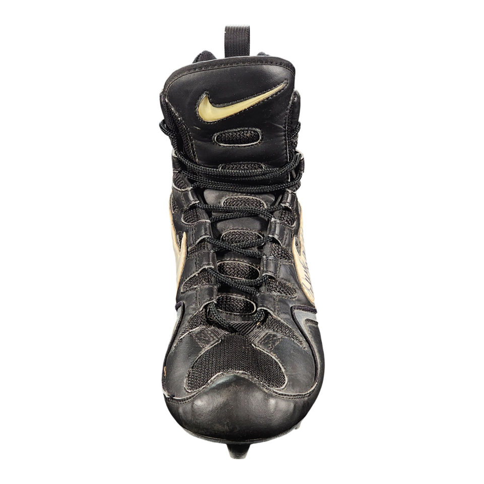 A black Nike high-top baseball cleat with gold accents, featuring a leather and mesh upper, lace-up front, and a spike on the sole, shown against a plain white background.