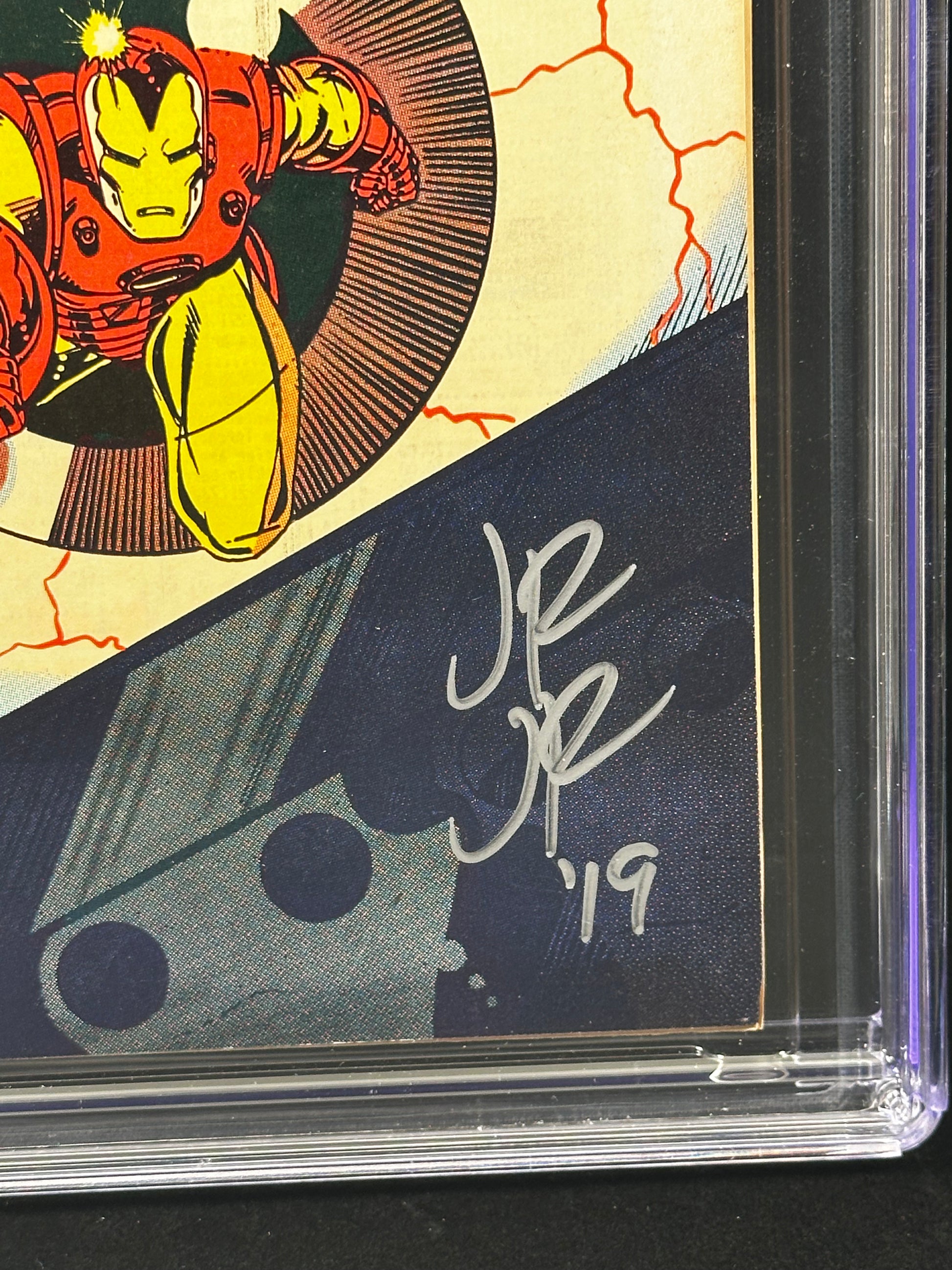 Close-up of a signed comic book card inside a clear protective case, featuring Iron Man artwork and a white autograph of John Romita Jr.